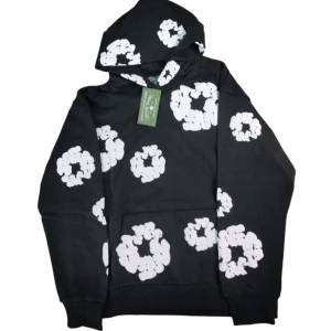 Denim Tears hoodie - Svart hoodie från Denim Tears med stora vita blommönster över hela tröjan. Klassisk huva och känguruficka framtill. Perfekt för dig som vill sticka ut med en cool och unik stil.