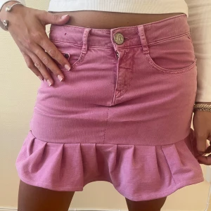 Rosa jeanskjol med volangkant - Supersöt rosa jeanskjol från replay med volangkant nertill. Kjolen har klassiska jeansfickor fram och bak, bälteshällor och stängs med knapp och dragkedja. Perfekt för dig som vill sticka ut med en färgglad och trendig look.