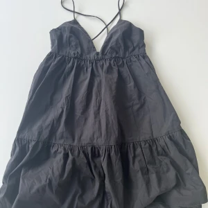 Svart klänning från Zara - Supersöt svart kort klänning från Zara med tunna axelband som korsas i ryggen och knyts. Klänningen har v-ringad urringning, volang nertill och öppen rygg. Den är i storlek S och i mycket bra skick.