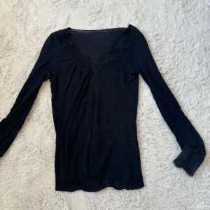 Svart långärmad topp med spets Intimissimi - Svart långärmad topp från Intimissimi med v-ringning och snygga spetsdetaljer vid halsringning och ärmslut. Bra kvalitet och inga defekter.