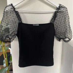 Unik topp! Med tyll och puffärmar! - Superfint skick! Säljer en svart topp med transparenta puffärmar i tyll med små svarta prickar. Toppen har rak halsringning och är figurnära i modellen. Perfekt för dig som vill ha något trendigt och unik! Svart topp med puffärmar och prickigt tyll! 