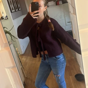 Mörklila stickad kofta med knyt - Säljer en mysig mörklila stickad kofta med två stora knytband framtill. Koftan har lång ärm och en loose passform, perfekt att slänga över en topp. Den är fluffig och har en enkel, stilren look.