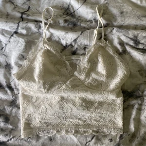 Vit spetstopp från Bik Bok - Supersöt vit linnetopp från Bik Bok med tunna axelband och v-ringad spetskant. Toppen är beige/vit typ och jag har tyvärr inte användning till den 🤍skriv för mer bilder eller funderingar 💋