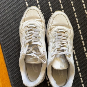 Vita Nike sneakers med snörning - Nike sneakers i helvitt med klassisk swoosh på sidan. Skorna har snörning, rund tå och platt sula. Ovandelen är i syntet och textil, med meshdetaljer för extra komfort. Perfekta för dig som gillar en clean och sportig look.