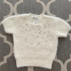 Vit fluffig stickad tröja från Zara - Stickad tröja från Zara som är köpt i ett annat land. Har diamanter på framsidan av tröjan. Lappen sitter kvar på tröjan. Har provat 1 gång men sedan inte kommit till användning. 