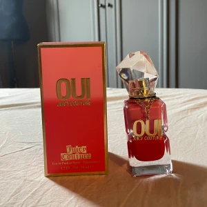 Juicy Couture Oui Eau de Parfum 50ml - Juicy Couture Oui är en parfym i en lyxig glasflaska med tvådelad design i rosa och rött, dekorerad med en stor kristallformad kork och guldfärgad kedja. Det är en 50ml flaska, med noter av citron, vattenmelon. Inslag av açaibär och toppnotering av päron, indisk tobros, jasmin och kaprifol.