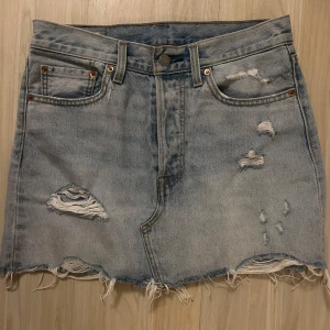 Levi's ljusblå jeanskjol med slitningar - Ljusblå jeanskjol från Levi's med rå kant och slitna detaljer framtill och baktill. Klassisk femficksmodell med knapp och dragkedja. Perfekt för dig som gillar en avslappnad och trendig look. Har aldrig använt köpte för 1300kr säljer den för 300kr 