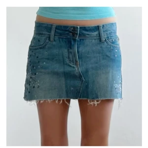 Blå jeanskjol med slitna kanter - Snygg blå jeanskjol med råa, fransiga kanter och små nitar som ger en cool vibe. Klassisk femficksmodell med bälteshällor och knappstängning framtill. Perfekt för dig som gillar en avslappnad och trendig stil.