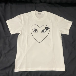 Comme des Garçons T-shirt  - En riktigt snygg vit T-shirt från Comme des Garçons. Med en svart logga på framsidan av tröjan på bröstet. Samt en broderad logga på  vänster sida av bröstet. | Den är så gott som ny i skicket 9,5/10. | Det är bara att höra av sig om man har några frågor🤍🤍🤍
