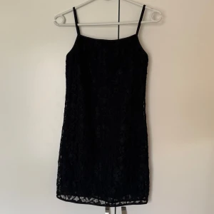 Svart spetsklänning  - Svart kort klänning med smala axelband och blommig spets över hela. Figurnära passform. Jättefint skick!