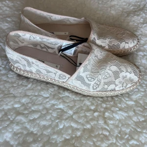 Beige spetsiga espadrillos från Zara - Snygga espadrillos från Zara i beige med vacker spets och blommigt mönster. Skorna har platt sula med klassisk flätad kant och rund tå. Perfekta för en somrig och avslappnad look.