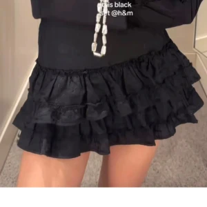 Svart volangkjol från H&M - Supersöt svart kortkjol från H&M med flera lager volanger som ger en riktigt trendig och lekfull look. Perfekt att styla med en croppad topp eller stickad tröja. Kjolen har en tight passform i midjan och är tillverkad i ett lätt material.