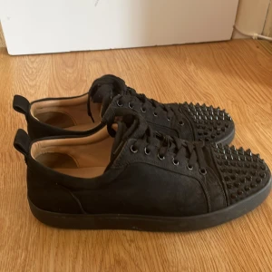Christian Louboutin svarta sneakers med nitar - Svarta sneakers från Christian Louboutin med ikoniska röda sulor och svarta nitar på, bra skick på dom och kan gå ner i pris vid snabbt köp.