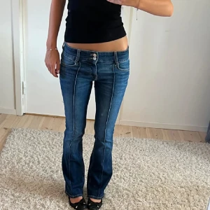 Blå bootcut jeans med låg midja - Snygga blå jeans med bootcut och låg midja. Jeansen har markerade sömmar framtill, dubbla knappar i midjan och klassisk femficksdesign. Materialet är jeans med lätt tvättad effekt och stretch för skön passform.