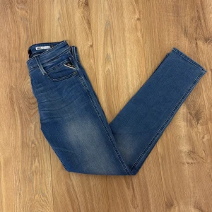 Replay Anbass slim fit jeans blå - Snygga blå Replay Anbass jeans i slim fit med klassisk femficksdesign och coola detaljer som logga på fickan och läderpatch bak. Jeansen har en lätt tvättad look och sitter tajt men bekvämt. Perfekta för dig som gillar stilrena och moderna jeans.