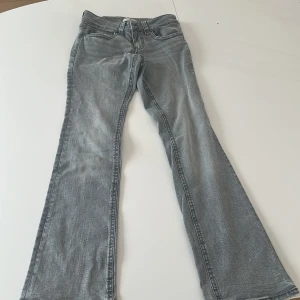 Grå bootcut jeans från Gina Tricot - Säljer dessa helt  oanvända snygga grå jeans från Gina Tricot i storlek 40 med bootcut-modell. Jeansen har klassiska fickor bak och silverfärgade knappar. De är tillverkade i mjukt denimtyg och har en cool tvättad look. 