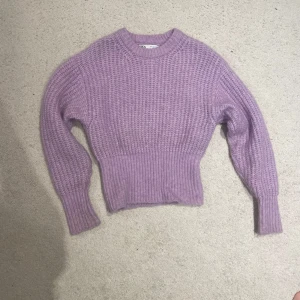 Ljuslila stickad tröja från Zara - Superfin ljuslila stickad tröja från Zara med bred ribbad midja och ärmslut. Tröjan har en mysig, fluffig känsla och en klassisk rund halsringning. Perfekt för dig som gillar en söt och trendig look. 