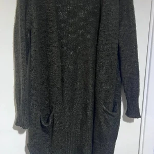 Mörkgrå stickad kofta Gina Tricot - Lång och mysig mörkgrå stickad kofta från Gina Tricot. Koftan har långa ärmar, två fickor framtill och en öppen front. Perfekt att slänga på sig över en t-shirt eller topp för en chill look.