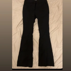 Svarta bootcut kostymbyxor - Svarta kostymbyxor med bootcut-silhuett och klassisk passform. Byxorna har hög midja och vida ben nertill, vilket ger en snygg och trendig look. Perfekta att styla med sneakers eller klackar. Materialet känns mjukt och följsamt.