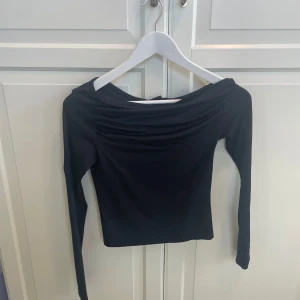 Svart långärmad topp Gina Tricot XS - Säljer en svart långärmad topp från Gina Tricot i storlek XS. Toppen har en snygg draperad urringning och är figurnära i modellen. Perfekt att styla med jeans eller kjol för en trendig look.