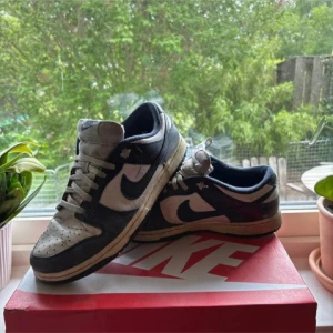 Nike Dunk Low i marinblått och vitt - Skorna säljs och skickas med original box. Nike Dunk Low sneakers i marinsblått och vitt med klassisk swoosh på sidorna. Skorna har snörning, perforerad tå och vadderad kant för extra komfort. Ovandelen är i skinn och textil, med en platt sula och rund tå. Perfekt för dig som gillar streetwear och retrostil.