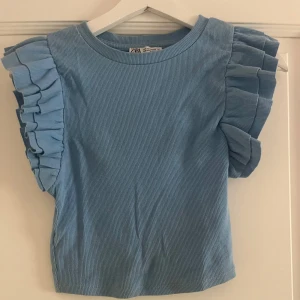 Blå volangtopp från Zara - Supersöt blå topp från Zara med ribbad struktur och stora volangdetaljer på axlarna. Passar både xxs, xs och s