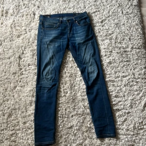 Blå jeans från Dondup - Snygga blå jeans från Dondup i modellen George  Fit. Jeansen har klassisk femficksdesign, orangea sömmar och en cool tvätt med lätt slitning. Materialet är stretchigt jeans och passformen är tight med smal siluett. Perfekt för dig som gillar en modern look.