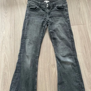 Grå low waisted bootcut jeans med dubbla knappar från Gina tricot young  - Snygga grå jeans med low waisted bootcut passform och dubbla knappar i midjan. Jeansen har klassiska fem fickor, bakfickor med lock och knapp, samt en cool tvättad look. Perfekta för dig som gillar en avslappnad stil med lite edge.