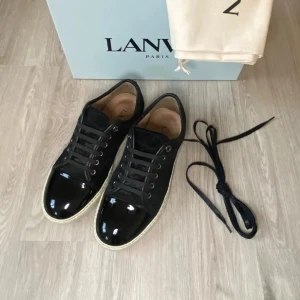 Lanvin Sneakers - Snygga svarta sneakers från Lanvin med blank tå i lack och ovandel i mocka. Skorna har svarta snören, metallöglor och en vit platt sula som ger en clean kontrast. Perfekta för dig som gillar stilrena och lyxiga detaljer.