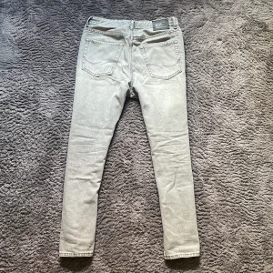 Grå straight fit jeans från Jack & Jones - Snygga grå jeans från Jack & Jones med klassisk femficksdesign och normal passform. Jeansen har en modern straight stil och är tillverkade i mjukt bomullsmaterial med lite stretch för extra komfort. Perfekt för dig som gillar en stilren och enkel look.