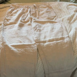 Beigea linnebyxor  från H&M - Snygga och chill beige linnebyxor från H&M med elastisk midja och snörning. Byxorna har en rak passform och är gjorda i mjukt linne, perfekt för varma dagar. Fickor på sidorna och avslappnad vibe. Passar dig som gillar enkel och clean stil.