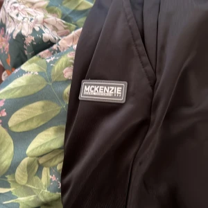 Svarta McKenzie mjukisbyxor L - Svarta mjukisbyxor från McKenzie med elastisk midja och diskret logga på benet. Byxorna har en clean look och är gjorda i ett mjukt syntetmaterial som känns skönt mot huden. Perfekta för chill eller träning, och har en loose passform för extra komfort.