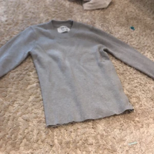 Grå ribbad tröja från Zara - Snygg grå långärmad tröja från Zara i ribbad bomull. Enkel och stilren design med rund hals och smal passform. Perfekt att matcha med jeans eller kjol för en chill look. Passar dig som gillar basic och neutrala färger.