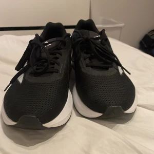 Adidas Duramo SL svarta sneakers strl 42 - Svarta Adidas Duramo SL sneakers med vita detaljer och klassiska ränder på sidan. Skorna har ventilerande mesh-ovandel, snörning och en tjock vit platt sula som ger skön dämpning. Perfekta för dig som gillar sportig stil och vill ha bekväma skor till träning eller häng.