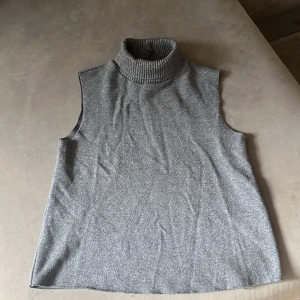 Grå ärmlös polotröja från Zara - Säljer en stilren grå polotröja från Zara i storlek S. Tröjan är ärmlös med en bred, ribbad polokrage och har en mjuk stickad känsla. Perfekt att styla med lager på lager eller som den är för en clean look.