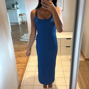 Blå långklänning med slits - Säljer en snygg blå långklänning med smockad struktur och breda axelband. Klänningen har en tight passform och en slits baktill. Klänningen är använd en gång och ser som ny ut.