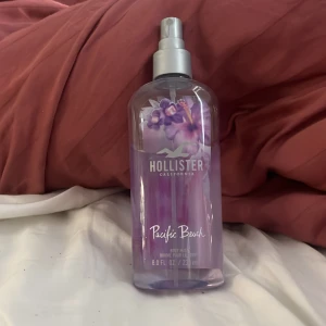 Hollister Pacific Beach Body Mist - Fräsch body mist från Hollister i doften Pacific Beach. Flaskan är genomskinlig med lila vätska och blommigt motiv på framsidan. Rymmer 236 ml och har en praktisk sprayfunktion. Perfekt för dig som gillar lätta, blommiga dofter.