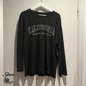 Svart långärmad tröja California - Svart långärmad tröja med trycket i vitt över bröstet. Tröjan har en loose passform och är gjord i mjuk bomull. Oversized