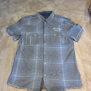 Blårutig kortärmad skjorta EDC Brand - Snygg blårutig skjorta från EDC Brand i storlek XL. Skjortan har korta ärmar, klassisk krage och två bröstfickor med knappar. Tillverkad i mjuk bomull och har vita knappar framtill. Perfekt för dig som gillar en chill och stilren look.