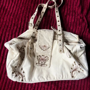 Beige axelväska med broderi från St. Sulpice - Snygg vintage beige axelväska från St. Sulpice med coola broderade detaljer i brunt och ljusrosa. Väskan har två justerbara axelremmar med nitar och spännen, samt dragkedja upptill. Perfekt storlek för allt du behöver och unik design som sticker ut💋💋💋
