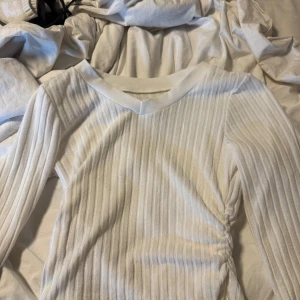 Vit ribbad långärmad tröja M - Säljer en vit ribbad långärmad tröja från MYV i storlek M. Tröjan har v-ringad hals och är tillverkad i mjuk polyester med lite stretch för en slim passform. Perfekt att styla med jeans eller kjol för en clean look.