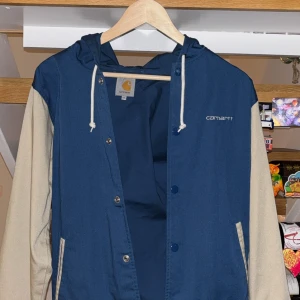 Blå och beige Carhartt bomberjacka S - Snygg bomberjacka från Carhartt i blått med beige ärmar och vit snörning i huvan. Jackan är aldirg använd endast testad.