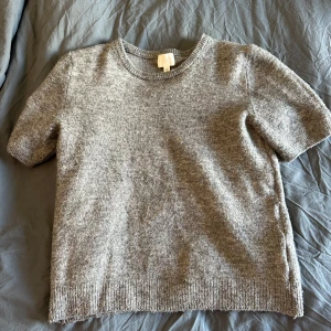 Grå stickad tröja från H&M - Mysig grå stickad tröja från H&M med korta ärmar och rund hals. Den är i väldigt fint skick, lite nopprig men inget man tänker på. Använd gärna köp nu och hör av er vid frågor!💓