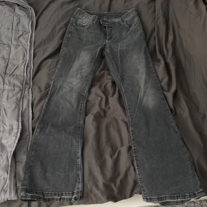 Bootcut svarta jeans med låg midja - Säljer ett par gråa bootcut jeans med låg midja och klassisk femficksdesign. Jeansen har en lätt tvättad look och raka ben som blir vidare nedtill. Materialet är jeans och färgen är mörkgrå/svart. Perfekt för dig som gillar retrovibbar och snygg siluett. Säljer dom för att dom börjar bli för små!