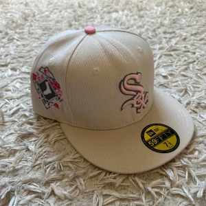 NEW ERA- Sox keps limited edition  - Snygg beige 59FIFTY keps från New Era med White Sox-logga i ljusrosa brodyr framtill och coolt broderat motiv på sidan. Platt skärm och rosa detalj på toppen. Perfekt för dig som vill sticka ut med sportig stil och unika detaljer. Den är limited edition- helt oanvänd och ny. Säljer pga för stor storlek. Den är helt perfekt som standout piece i ens outfit och är helt perfekt för sommarsolen men även vardagen. 