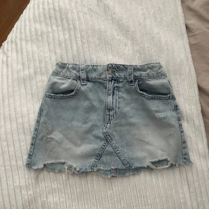 Ljus jeanskjol från Gina Tricot - Storlek 164 men skulle säga att den sitter som xs, Säljer en ljusblå jeanskjol från Gina Tricot i kort modell. Kjolen har slitna detaljer, fransad nederkant och snygga broderade bakfickor med knapp. Justerbar midja med resår och klassiska fickor fram. Perfekt för dig som gillar en chill och trendig stil.