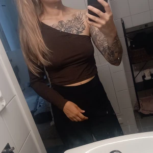 Brun oneshoulder långärmad topp - Säljer en brun långärmad topp med oneshoulder-design. Snygg croppad passform som visar axeln och ger en cool look. Perfekt för dig som gillar att sticka ut med enkla detaljer. Materialet känns mjukt och följsamt mot huden.