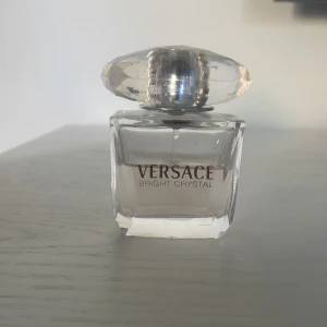 Versace Bright Crystal parfym - Versace Bright Crystal parfym i en elegant, transparent glasflaska med ett stort, diamantformat lock i plast. Flaskan har en lyxig och modern design med ljusrosa toner i vätskan. Perfekt för dig som gillar exklusiva dofter och snygga flaskor. Hälften är andvänd