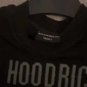 Svart Hoodrich sweatshirt med tryck - Svart sweatshirt från Hoodrich i storlek small med stort tryck på bröstet och coola grafiska detaljer på ryggen. Tröjan har två praktiska fickor framtill och långa ärmar. Perfekt för dig som gillar streetwear och vill sticka ut med snygga prints.
