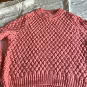 Rosa stickad tröja från H&M - Säljer en superfin rosa stickad tröja från H&M i storlek L. Tröjan har ett coolt bubbligt stickat mönster och ribbade muddar vid hals, ärmslut och nederkant. Perfekt för dig som gillar färg och vill ha en mysig look.